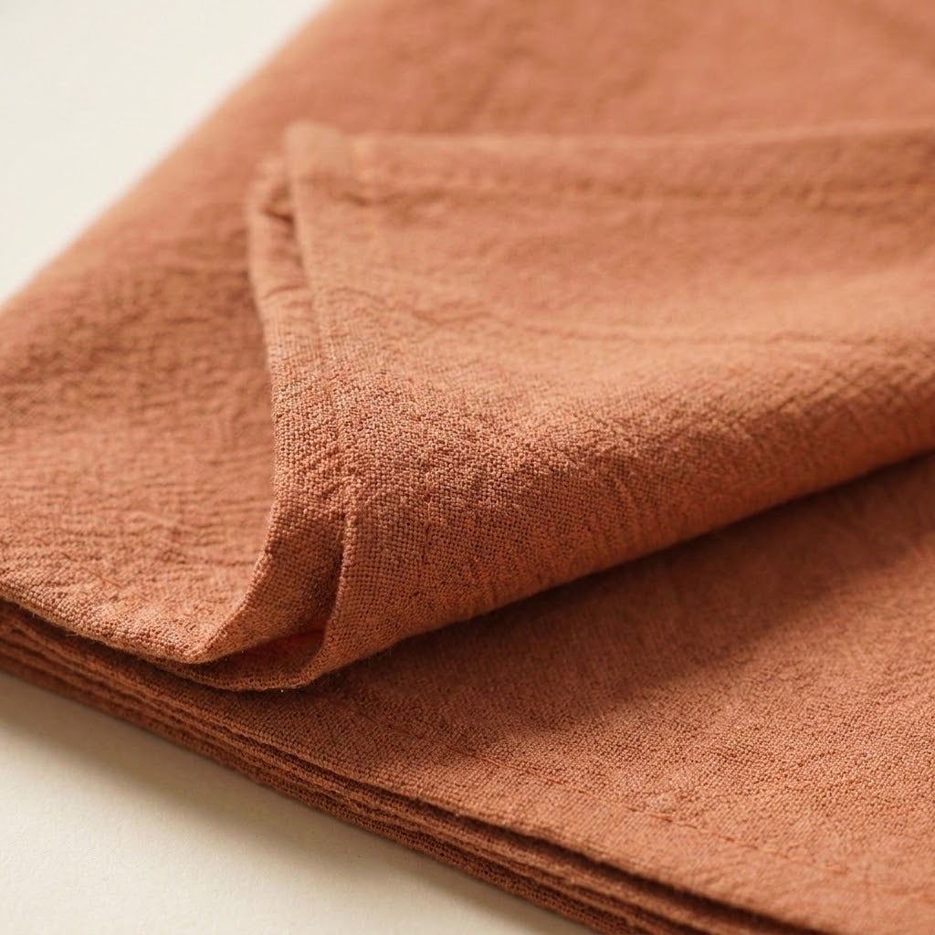 A close-up of folded terracotta-colored textured fabric, showing its woven linen-like pattern against a light neutral background.