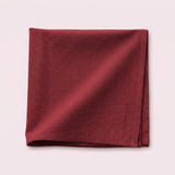 A folded square piece of textured fabric in a deep burgundy red, displayed on a solid pale pink background.