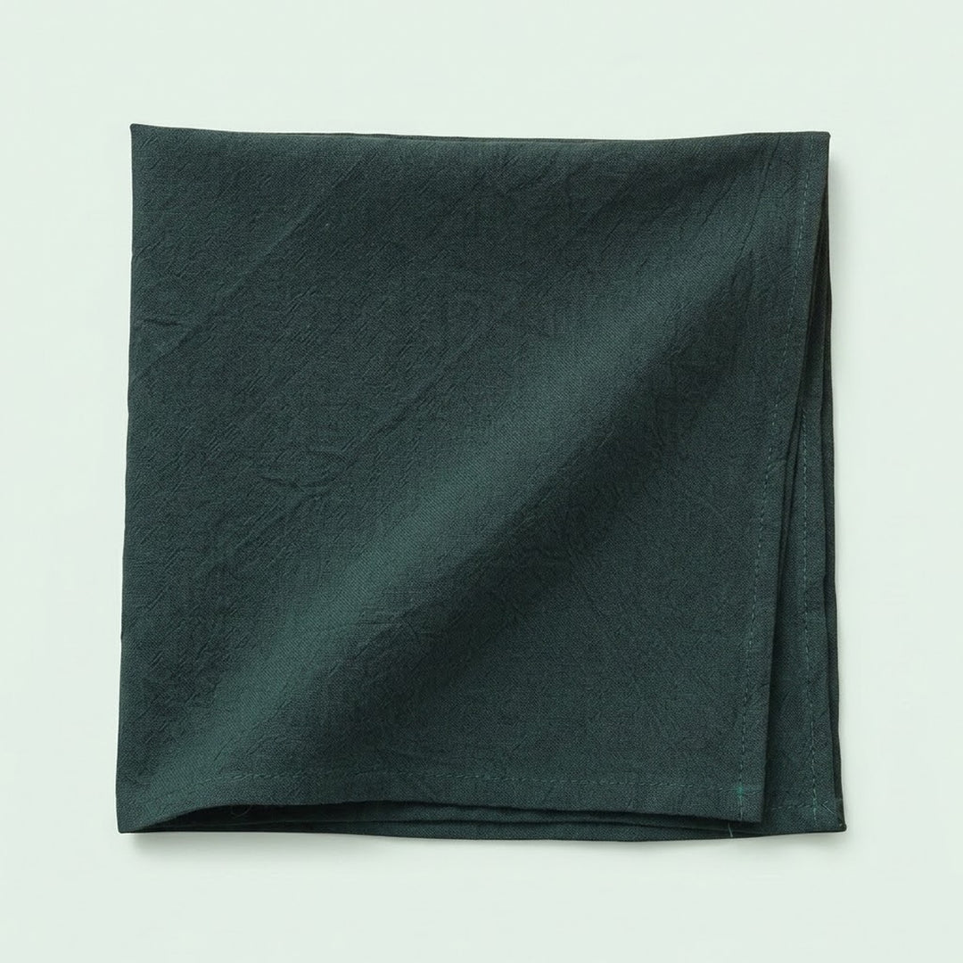A folded dark forest green fabric napkin or pocket square with a subtle crinkled texture, displayed on a light off-white background.