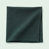 A folded dark forest green fabric napkin or pocket square with a subtle crinkled texture, displayed on a light off-white background.