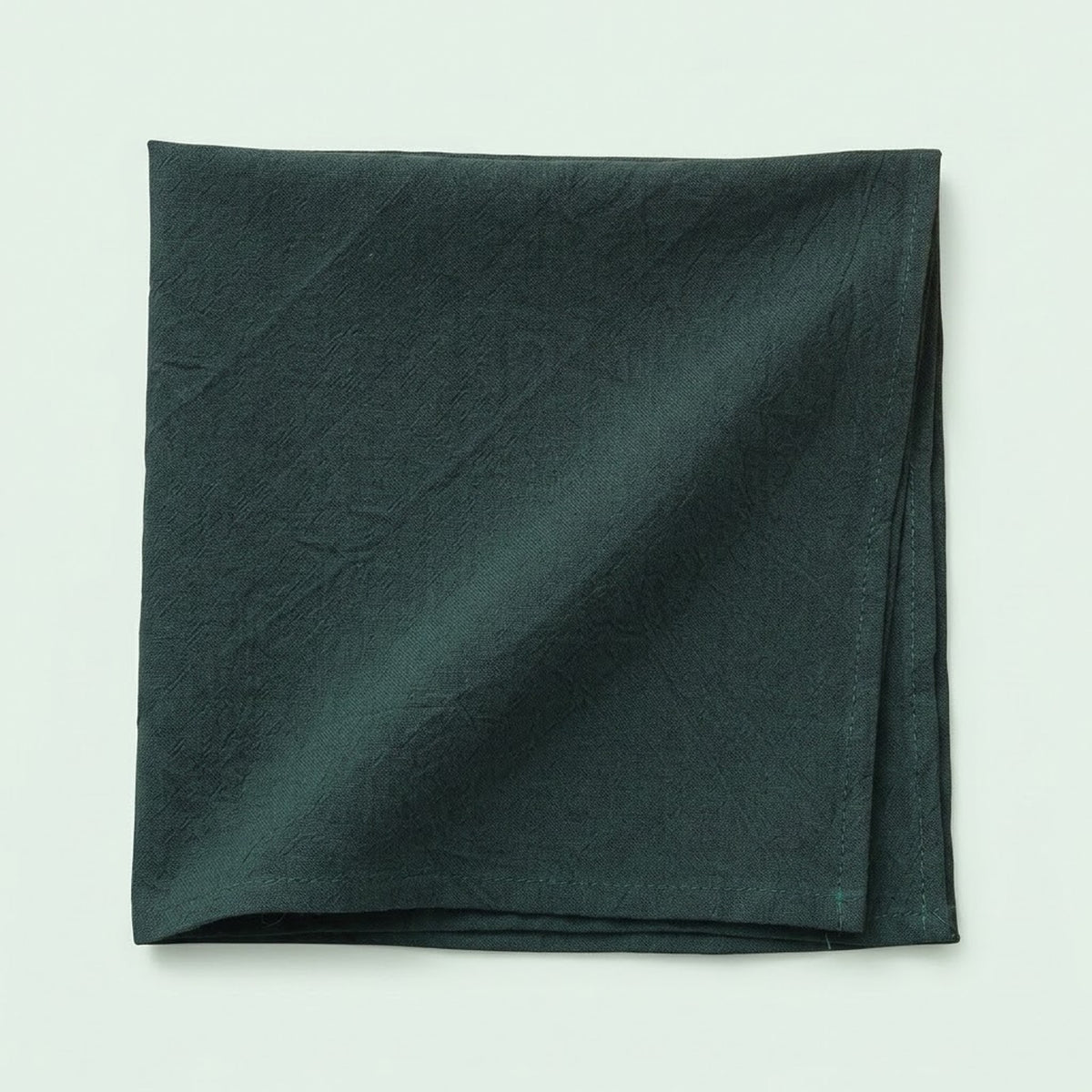 A folded dark forest green fabric napkin or pocket square with a subtle crinkled texture, displayed on a light off-white background.