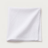 A folded white cotton napkin with a textured weave, displayed on a light beige background.