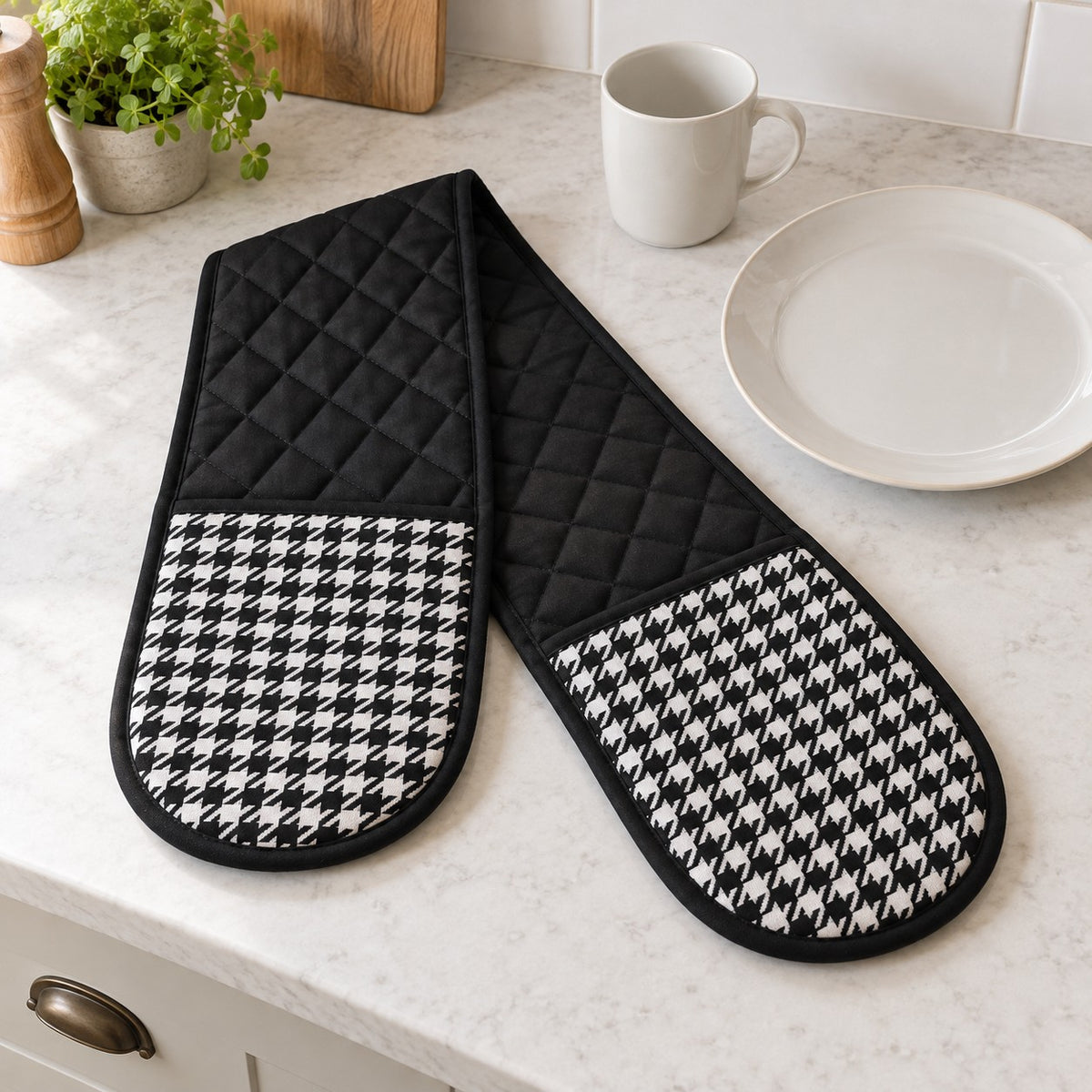 Black houndstooth double oven mitt beside a dinner plate and mug for scale.