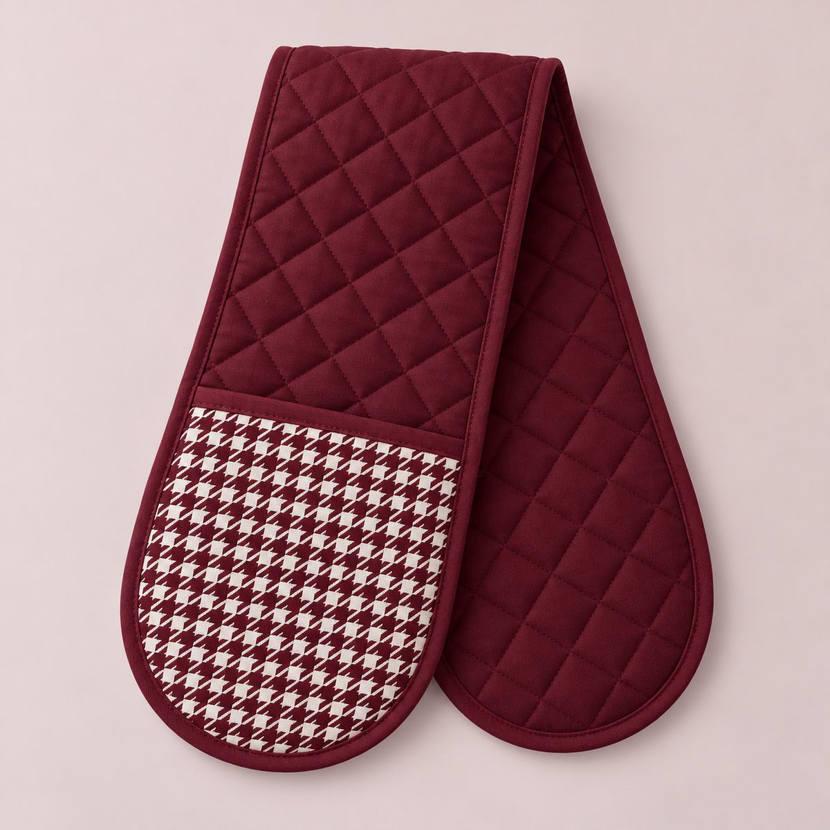 Burgundy quilted houndstooth double oven mitt centered on a pale rose studio background.
