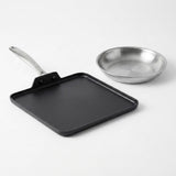 A square black non-stick griddle with a long handle and a small stainless steel frying pan, photographed on a clean white background.