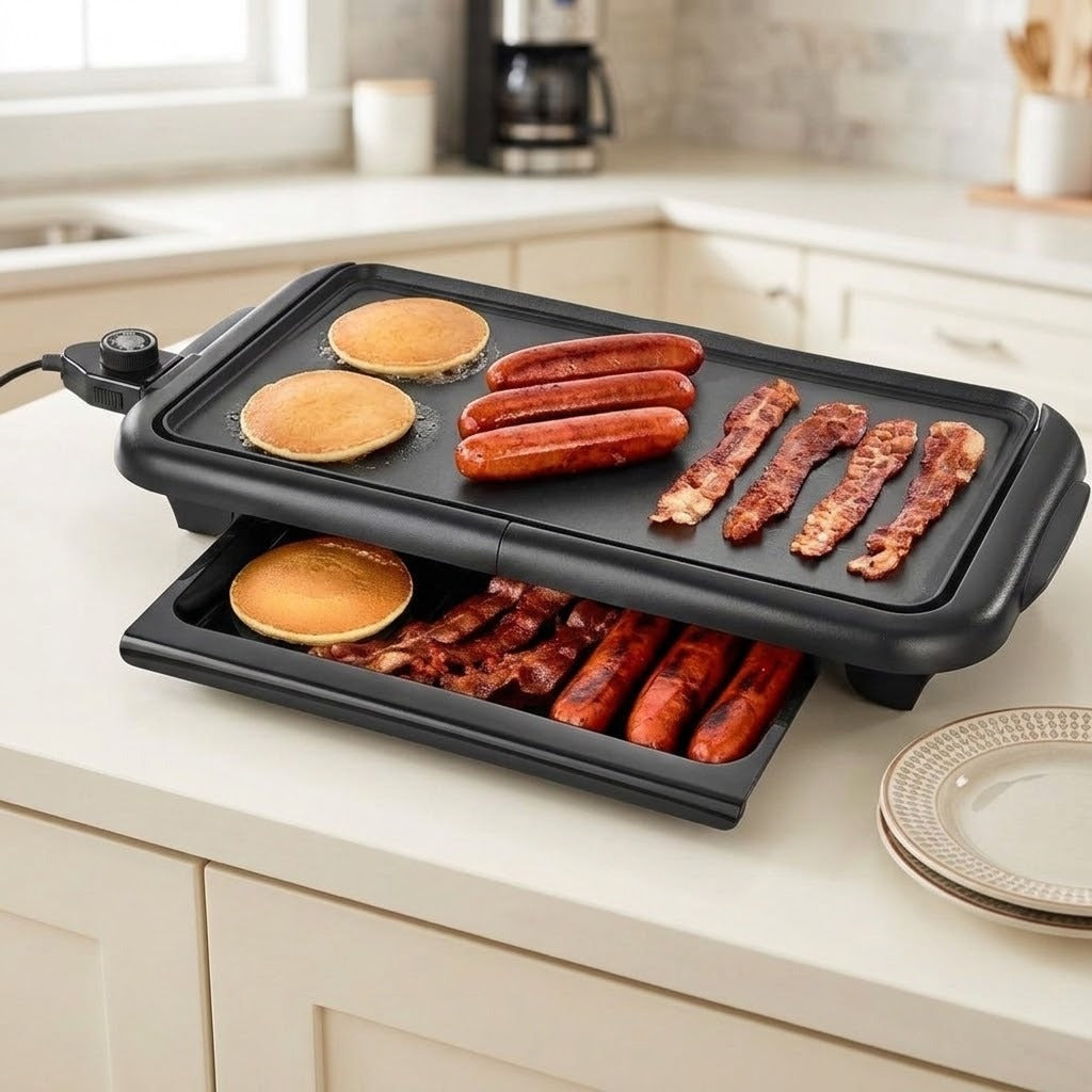 A black electric multi-cooker griddle with a raised lid, shown cooking pancakes, sausages, and bacon on a kitchen countertop.