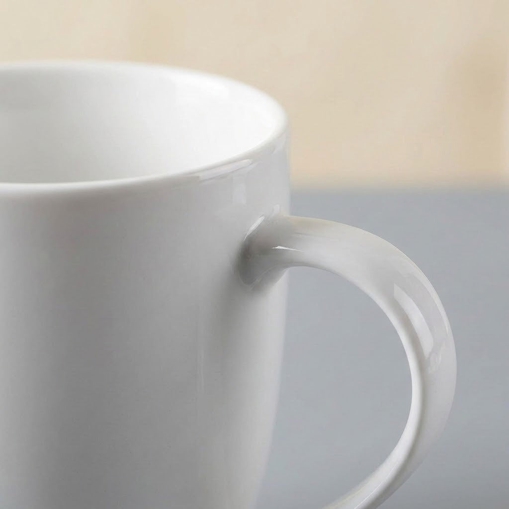 A close-up of a glossy white ceramic mug with a thick handle, set against a softly blurred background with a gray lower section and a light beige upper section.
