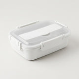 A white plastic lunch box with a clear lid and white latch closures, photographed on a clean light gray studio background.