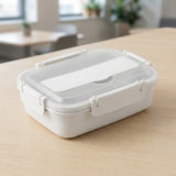 A white rectangular food storage container with a clear lid and secure latches, resting on a light wood table with a blurred indoor background.