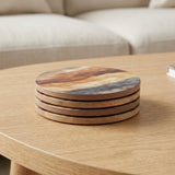 A stack of four round wooden coasters with a natural wood grain pattern, resting on a light oak table in a living room setting.