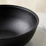 A close-up of a matte black ceramic bowl with a textured interior, resting on a light gray surface against a soft beige background.