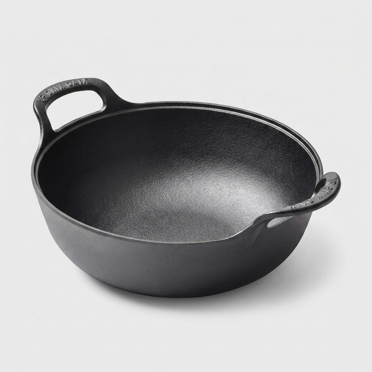 A black cast iron kadhai pot with two loop handles, photographed on a clean light gray background.