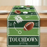 A football-themed table runner displayed on a wooden dining table. The runner features a green turf design with white yard line markings, footballs, helmets, and the words 'GAME TIME' and 'TOUCHDOWN'.