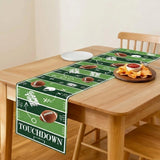A green football field themed table runner with white yard line markings, footballs, and the word 'TOUCHDOWN' is displayed on a wooden dining table with food props.