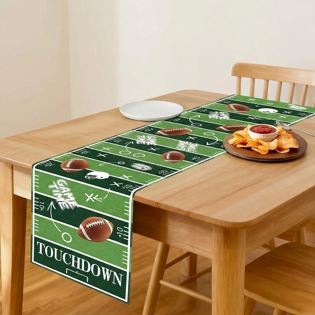 A green football field themed table runner with white yard line markings, footballs, and the word 'TOUCHDOWN' is displayed on a wooden dining table with food props.