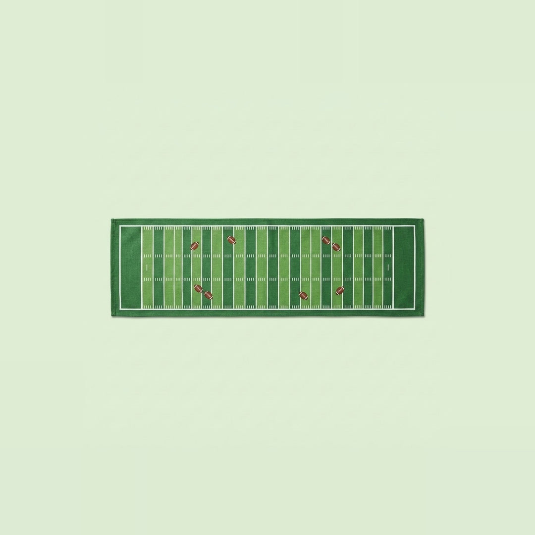 A rectangular green towel featuring a football field design with yard lines and small red accents, displayed flat against a pale green background.