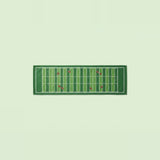 A rectangular green towel featuring a football field design with yard lines and small red accents, displayed flat against a pale green background.