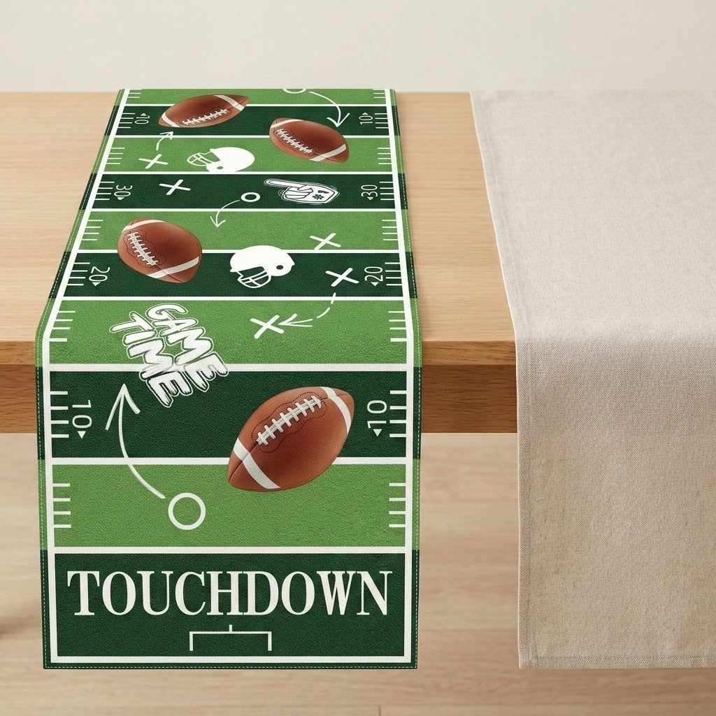 A green football-themed table runner with white yard-line markings, footballs, helmets, and the word 'TOUCHDOWN,' displayed on a light wood table next to a beige tablecloth.