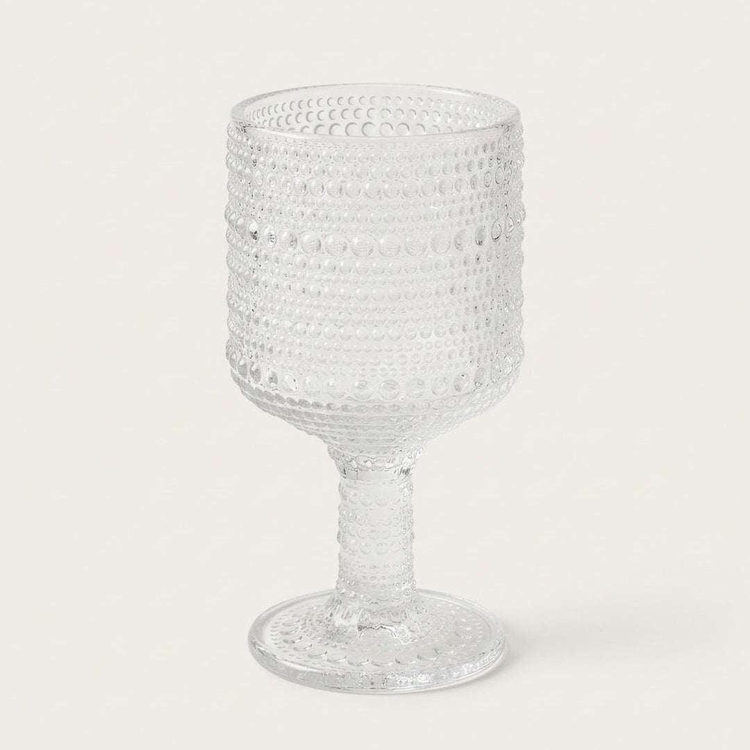 A clear textured glass goblet with a beaded, dotted pattern on the bowl and stem, set against a plain off-white background.