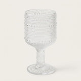 A clear textured glass goblet with a beaded, dotted pattern on the bowl and stem, set against a plain off-white background.