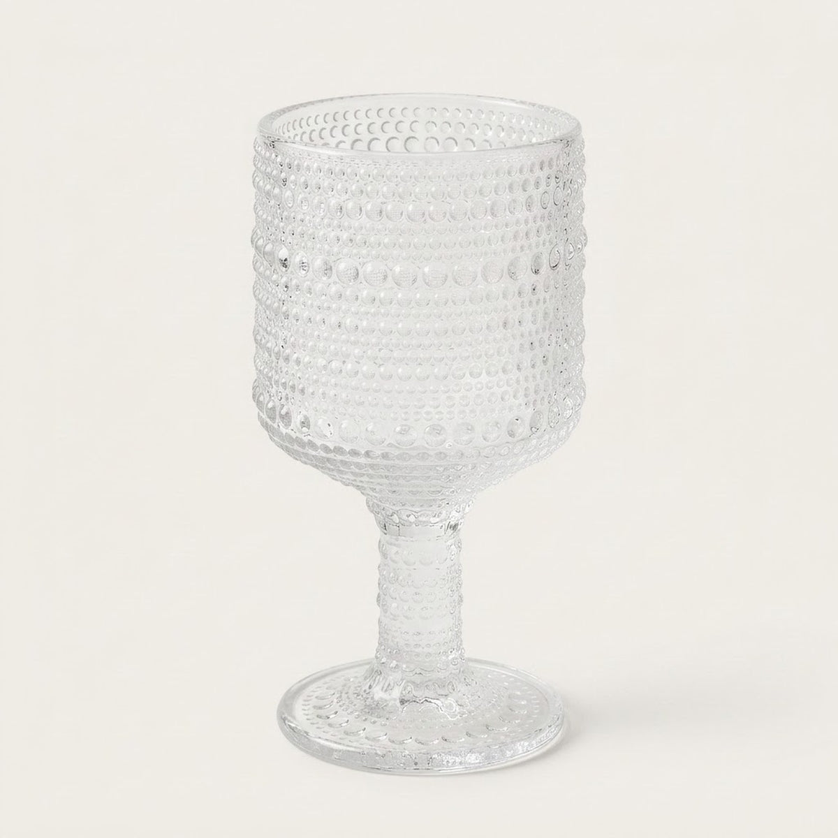 A clear textured glass goblet with a beaded, dotted pattern on the bowl and stem, set against a plain off-white background.