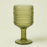 An olive green glass goblet with a textured, beaded pattern on the bowl and stem, set against a plain off-white background.