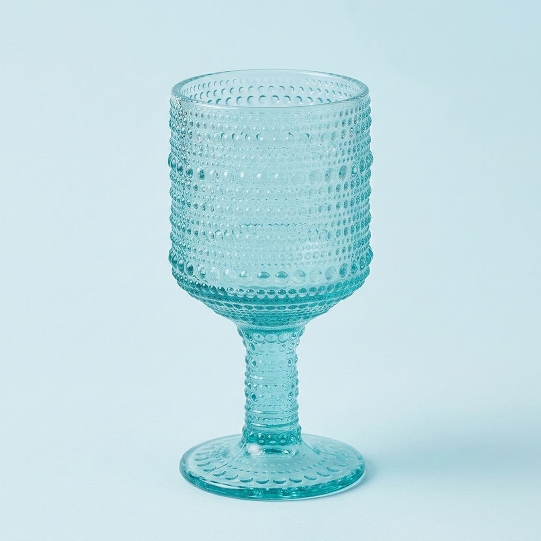 A light blue textured glass goblet with a dotted bubble pattern, set against a solid pale blue background.