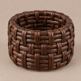 Dark brown basket weave rattan napkin ring shown alone on a soft taupe backdrop.