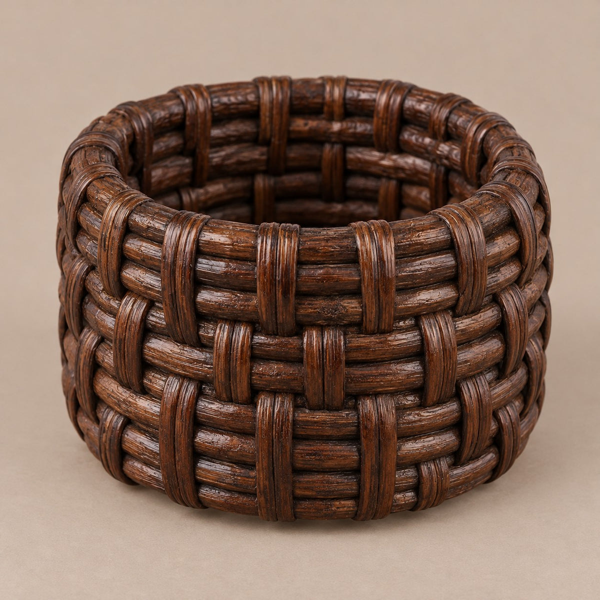Dark brown basket weave rattan napkin ring shown alone on a soft taupe backdrop.