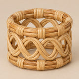 Natural open braid rattan napkin ring shown alone against a pale tan backdrop.