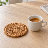 A round rattan coaster sits beside a small ceramic cup to show its compact scale.