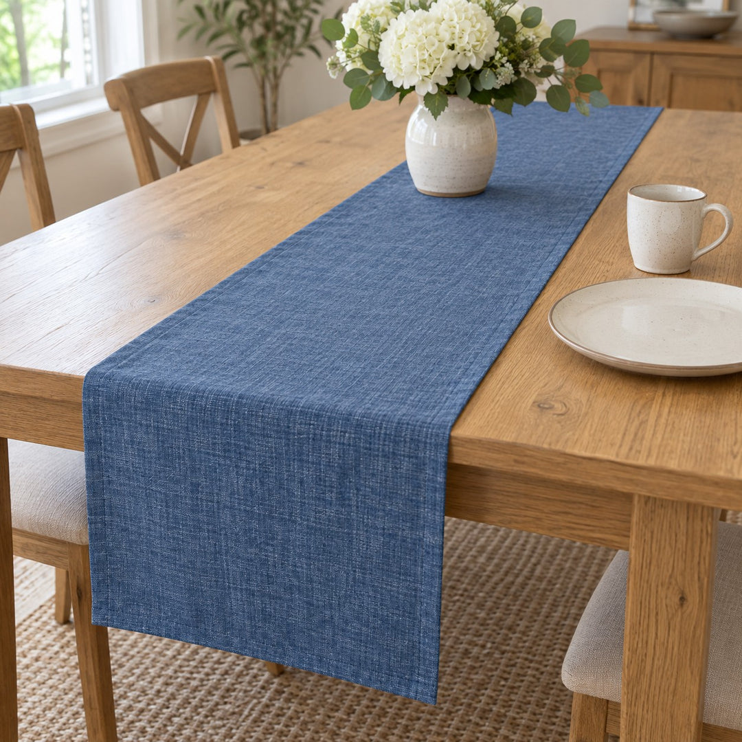 Blue rectangular linen table runner shown beside a dinner plate and cup for everyday scale.