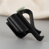 A black plastic hook-and-loop accessory with a small pale green circular accent, photographed on a neutral gray surface with a soft beige fabric background.