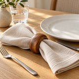 An acacia wood napkin ring dresses a folded linen napkin at an everyday dining place setting.