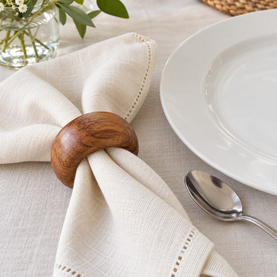 An acacia wood napkin ring beside a dinner plate shows its scale around a folded cloth napkin.