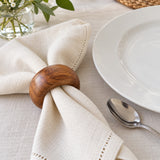An acacia wood napkin ring beside a dinner plate shows its scale around a folded cloth napkin.