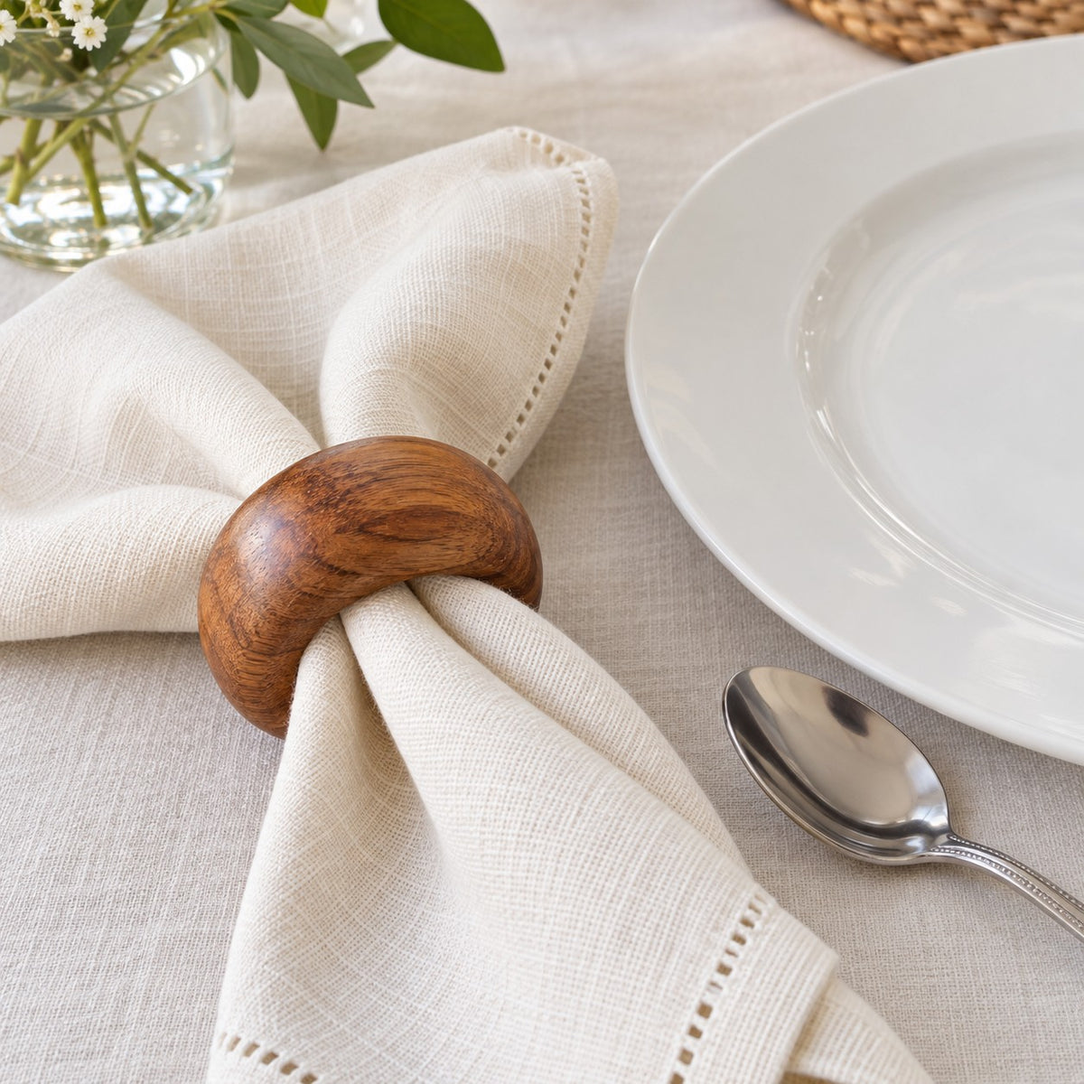 An acacia wood napkin ring beside a dinner plate shows its scale around a folded cloth napkin.