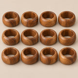 Set of 12 acacia wood napkin rings shown together against a light warm taupe background.