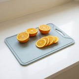 A light gray silicone cutting board with a handle, shown on a white countertop with several sliced oranges on top.