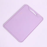 A light purple plastic cutting board with a built-in handle cutout in the top right corner, shown on a solid pale pink background.