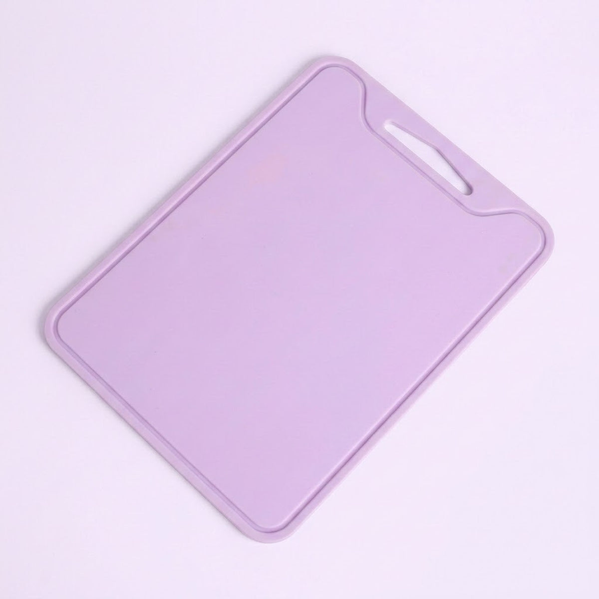 A light purple plastic cutting board with a built-in handle cutout in the top right corner, shown on a solid pale pink background.