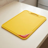 A yellow rectangular cutting board with a built-in handle, resting on a white kitchen countertop.