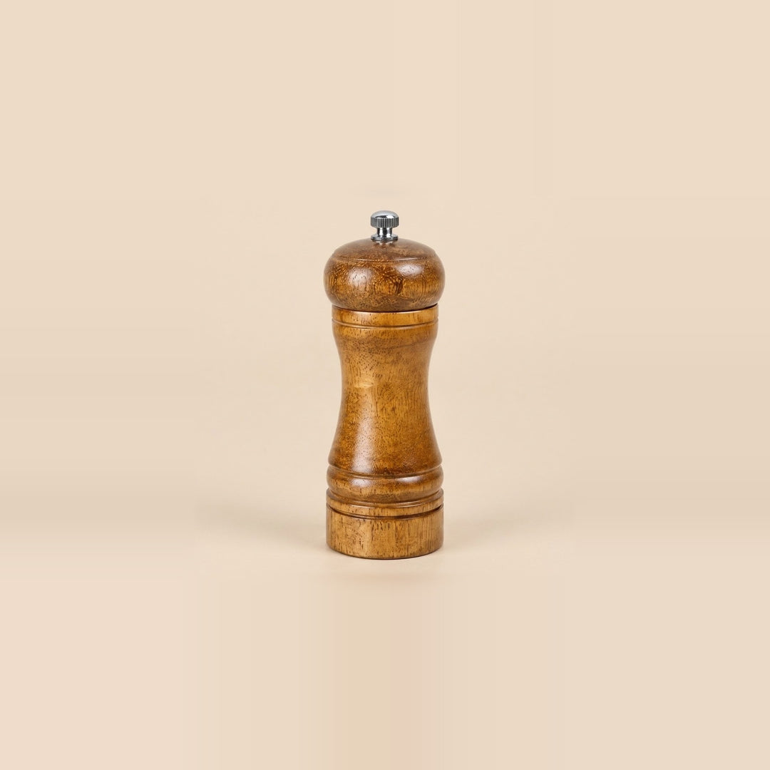 A classic wooden pepper mill grinder with a polished brown wood body and a small silver metal knob on top, set against a solid beige background.