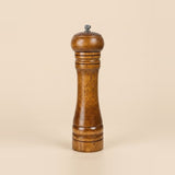 A single wooden pepper mill with a warm medium-brown finish and a small silver metal top knob, centered on a solid light beige background.