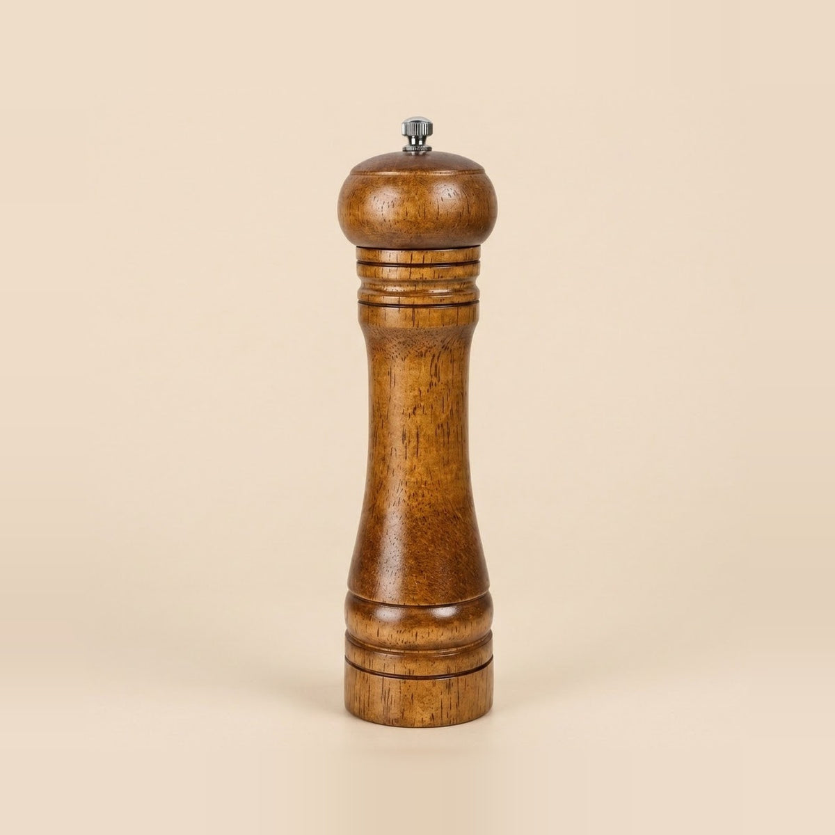 A single wooden pepper mill with a warm medium-brown finish and a small silver metal top knob, centered on a solid light beige background.