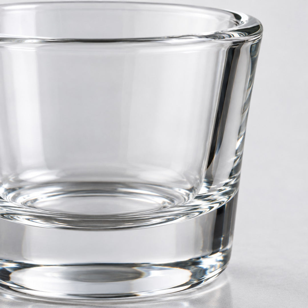 A macro view shows the smooth clear glass, polished rim, and thick base of a shot glass.