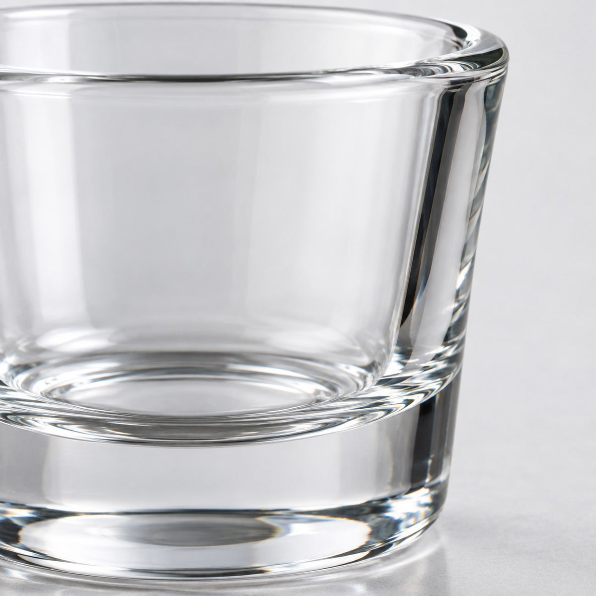 A macro view shows the smooth clear glass, polished rim, and thick base of a shot glass.
