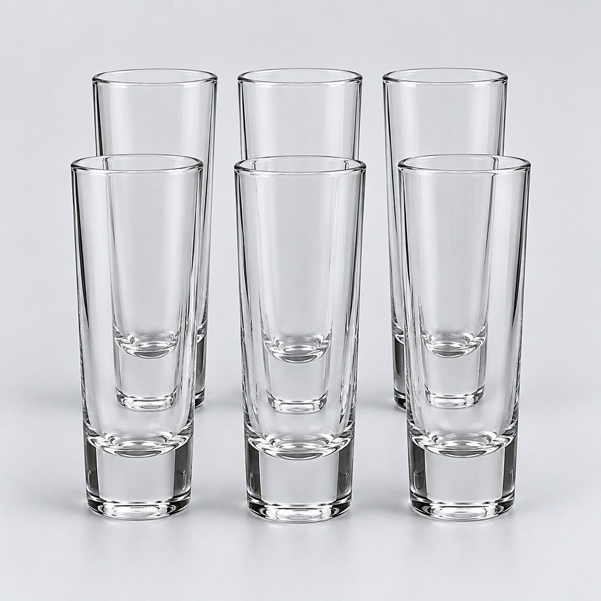 Six tall cylindrical clear glass shot glasses show the Tall Cylinder style on a pale backdrop.