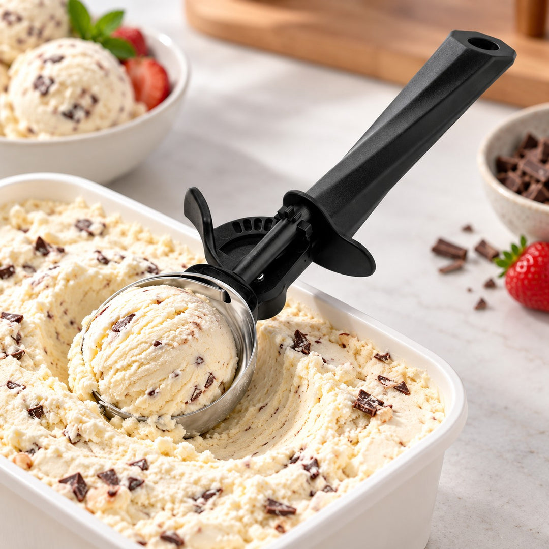 Ice cream scoop shapes a serving from a tub on a bright kitchen counter.