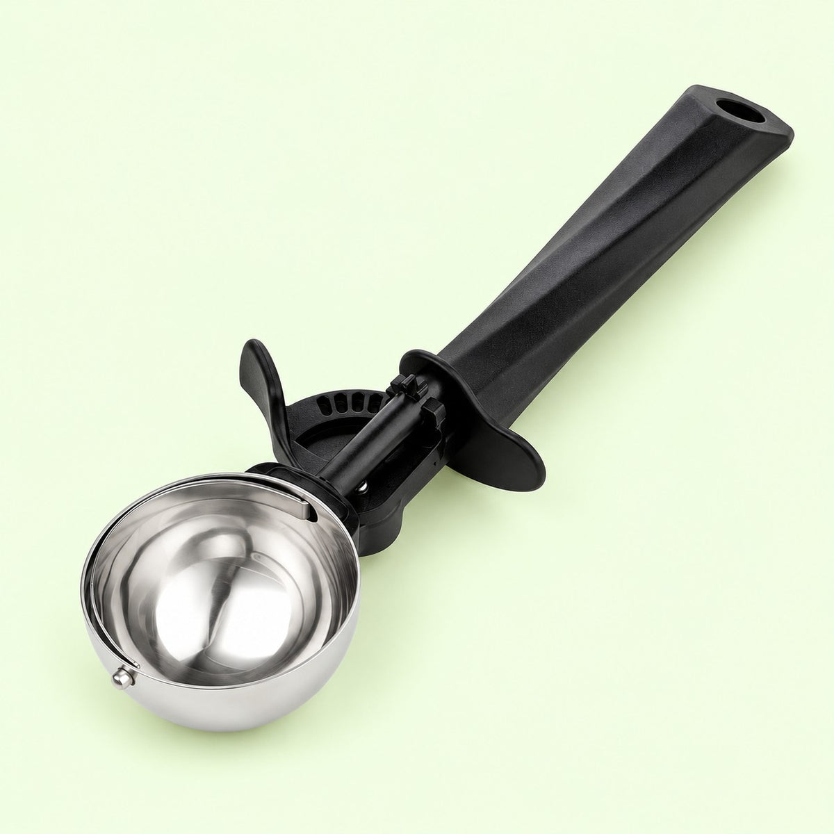 Medium ice cream scoop with polished steel bowl and black handle on a pale green backdrop.
